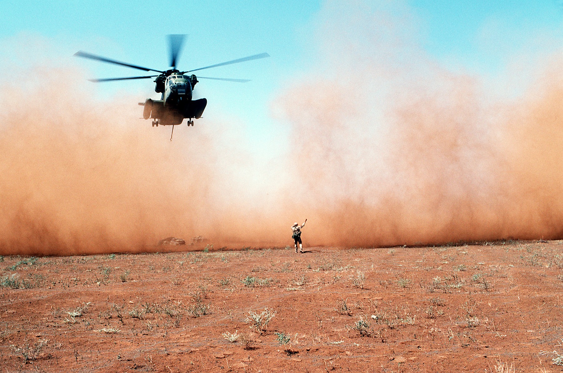 A Marine CH-53D Sea Stallion helicopter lifts off in a cloud of dust after delivering grain in Somalia.